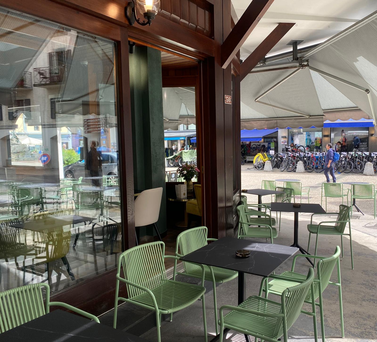 Les tables et fauteuils verts de la terrasse sous l’auvent